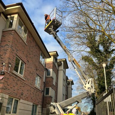 Worker cleaning gutters on a multi-story brick house using a Cherry picker