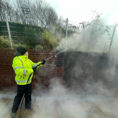 Worker performing stone and brick cleaning on an exterior wall using a steam cleaning method .